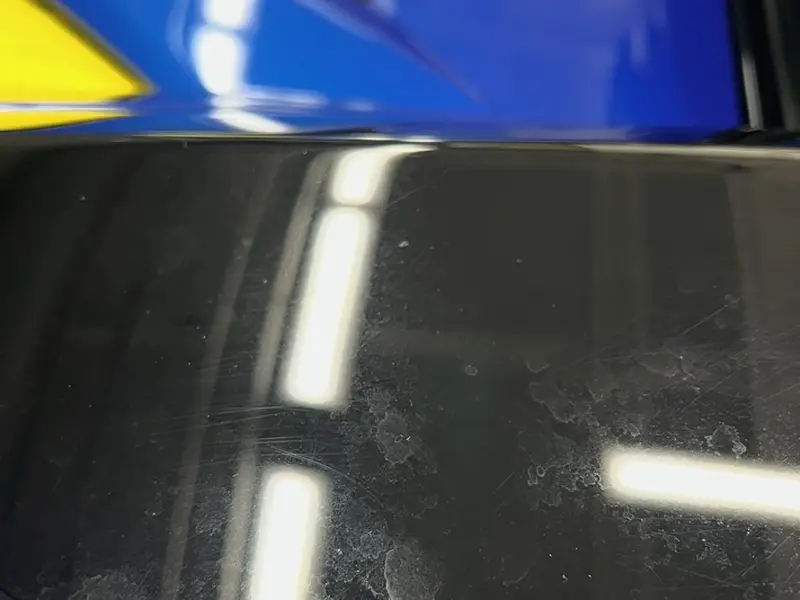Black engine panel with water spots and defects before correction